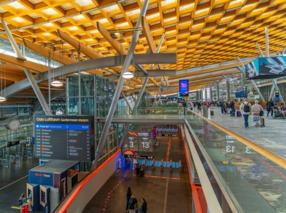 View of the interior of the departure lounge at Oslo Airport, with passengers, shops, and departure boards.