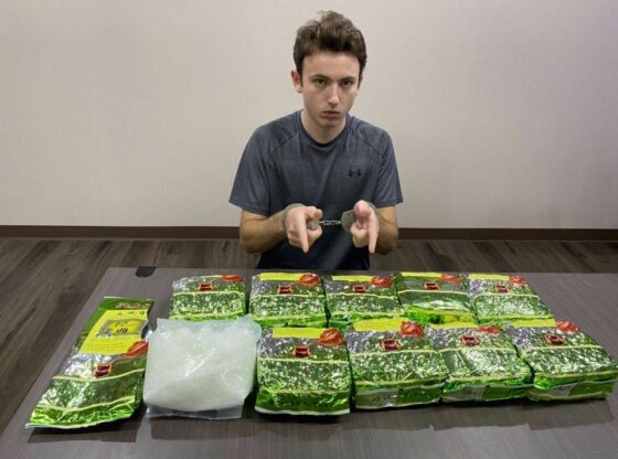 A man in handcuffs seated at a table with packages of crystal meth.