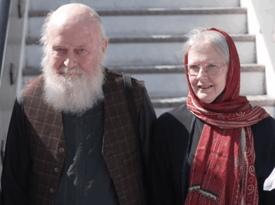 A bald man with a white beard and a woman with a red headscarf.