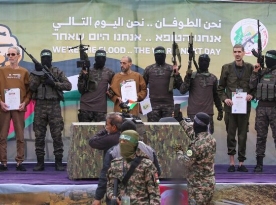 Ohad Ben Ami, Eli Sharabi, and Or Levy, holding certificates, escorted by Hamas fighters on a stage in Deir el-Balah, central Gaza.