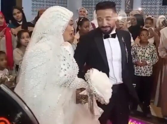 A groom in a tuxedo smiling and holding his bride's hand while dancing at their wedding.