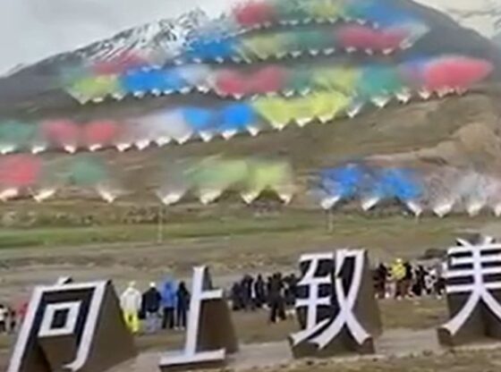 Fireworks display with multiple colorful plumes of smoke on a mountainside, above large white Chinese characters.