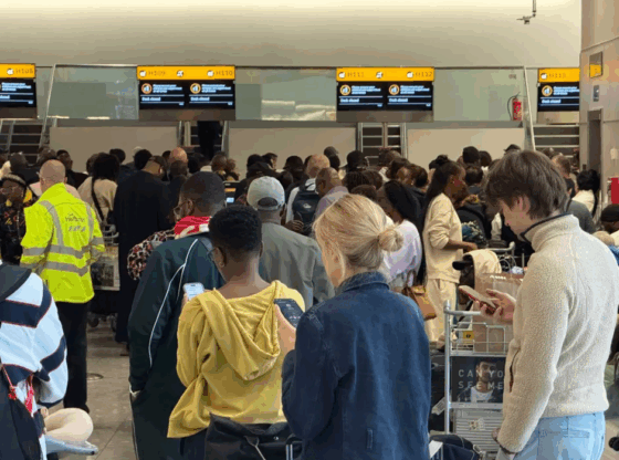 A crowded airport terminal with passengers in line and screens showing "Desk closed."