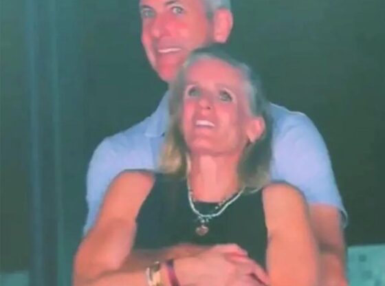 A man with gray hair embracing a woman with blonde hair from behind.