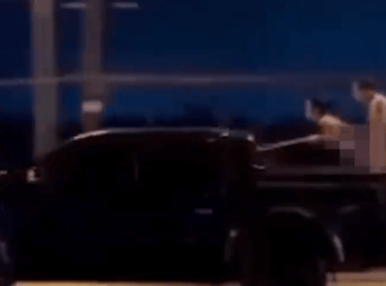 Two people with blurred bodies in the bed of a moving truck.