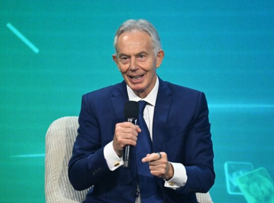 Tony Blair speaking into a microphone while sitting in a chair.