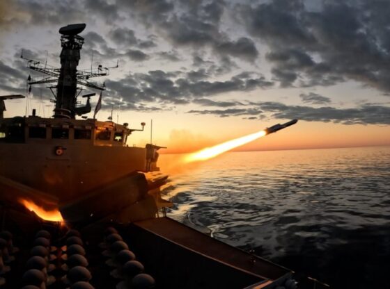 A frigate firing a missile over the ocean at sunset.