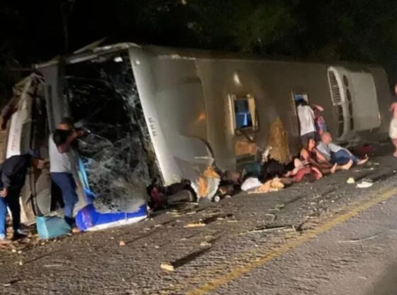 An image collage containing 1 images, Image 1 shows Overturned bus on its side with shattered windows and people nearby on the road following a crash