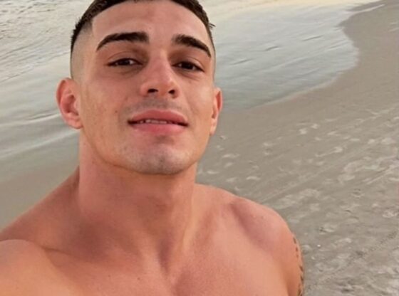 Flavio Augusto Schuller Azambuja smiling at the camera with the ocean and beach behind him.