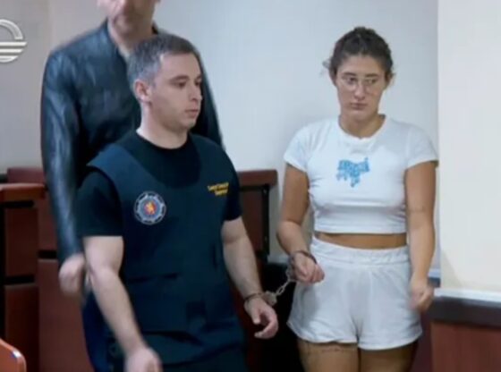 An image collage containing 1 images, Image 1 shows A woman in white shorts and t-shirt, handcuffed, stands in a courtroom next to a guard