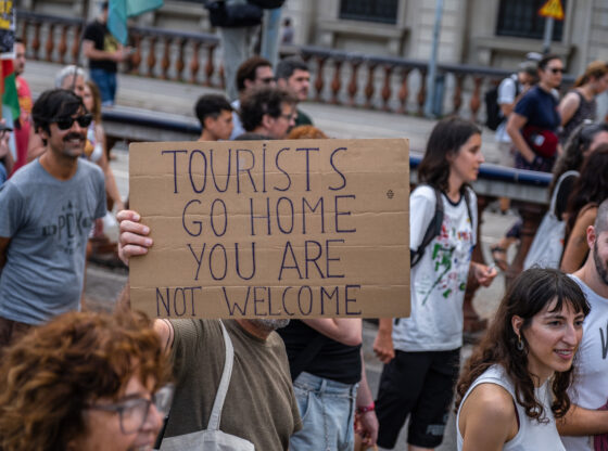 Protestor holding a sign that reads "Tourists go home you are not welcome."