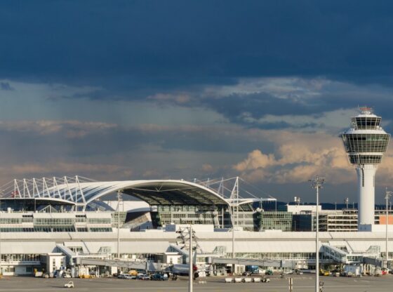 The Air Traffic Control Tower and building exterior of Munich Airport under a dark, cloudy sky.