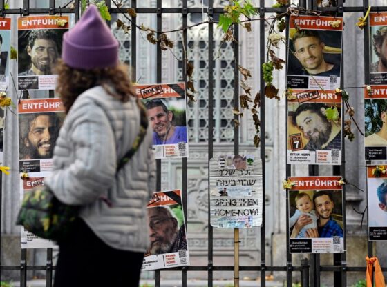 A woman passing by a fence covered with posters of Israeli hostages, mostly men, with the words "Bring them home now" and "Kidnapped" (abducted).