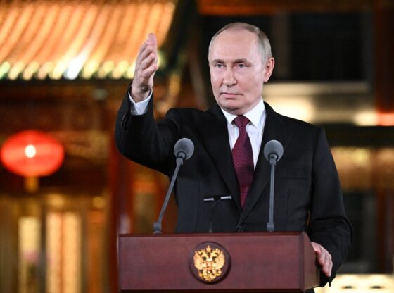 Russian President Vladimir Putin speaks at a podium with two microphones, gesturing with his right hand during a press conference in Beijing.