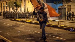 A protester with a large Peruvian flag, with the Police in the background.