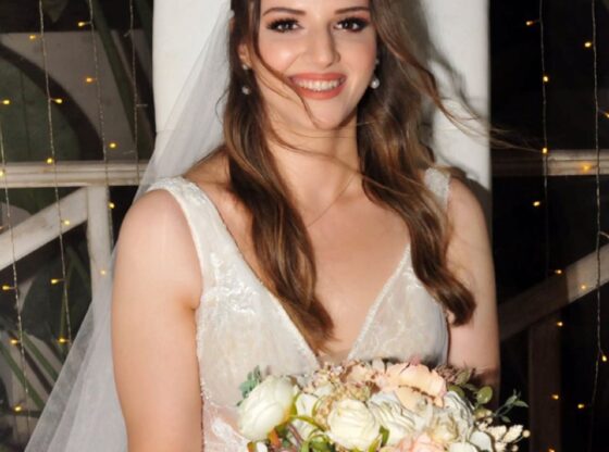 Pelin Kiyga in a white wedding dress, holding a bouquet of light-colored flowers.
