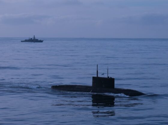 Russian Kilo-class submarine Novorossiysk on the surface of the sea with HMS Iron Duke frigate in the background.