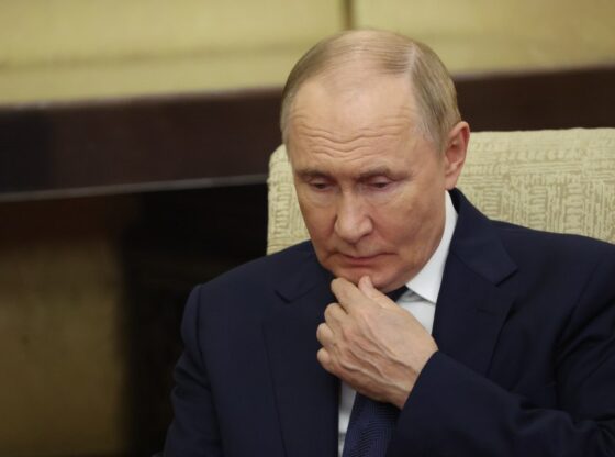 Russian President Putin in a dark suit, looking down with his hand on his chin.