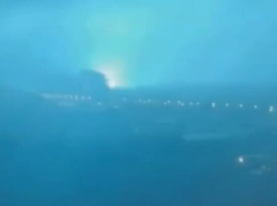 City skyline at night with a bright blue-green flash of light in the distance.