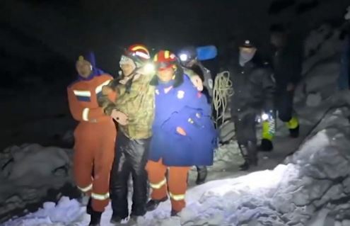 Rescuers in snow helping a stranded hiker at night with headlamps.