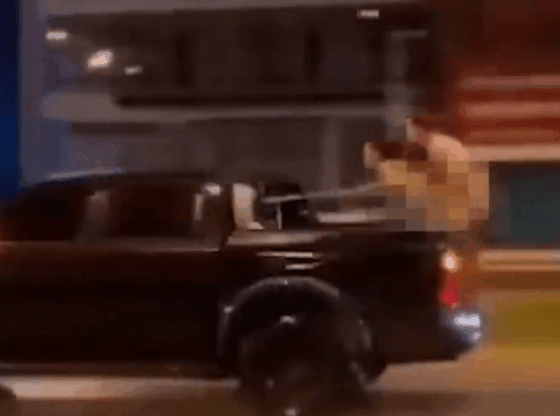 A person in the back of a moving pickup truck aims a gun.