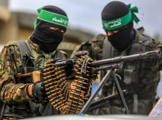 An image collage containing 1 images, Image 1 shows Two Hamas fighters with covered faces in camouflage secure an area before a hostage exchange